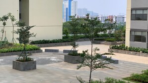 A courtyard with potted trees and a paved walkway, surrounded by modern buildings. - Brand New And Comfortable Studio At Daan Mogot City Apartment (Jakarta)