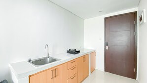 A small kitchen with a sink, a stove, and wooden cabinets. - Brand New And Comfortable Studio At Daan Mogot City Apartment (Jakarta)