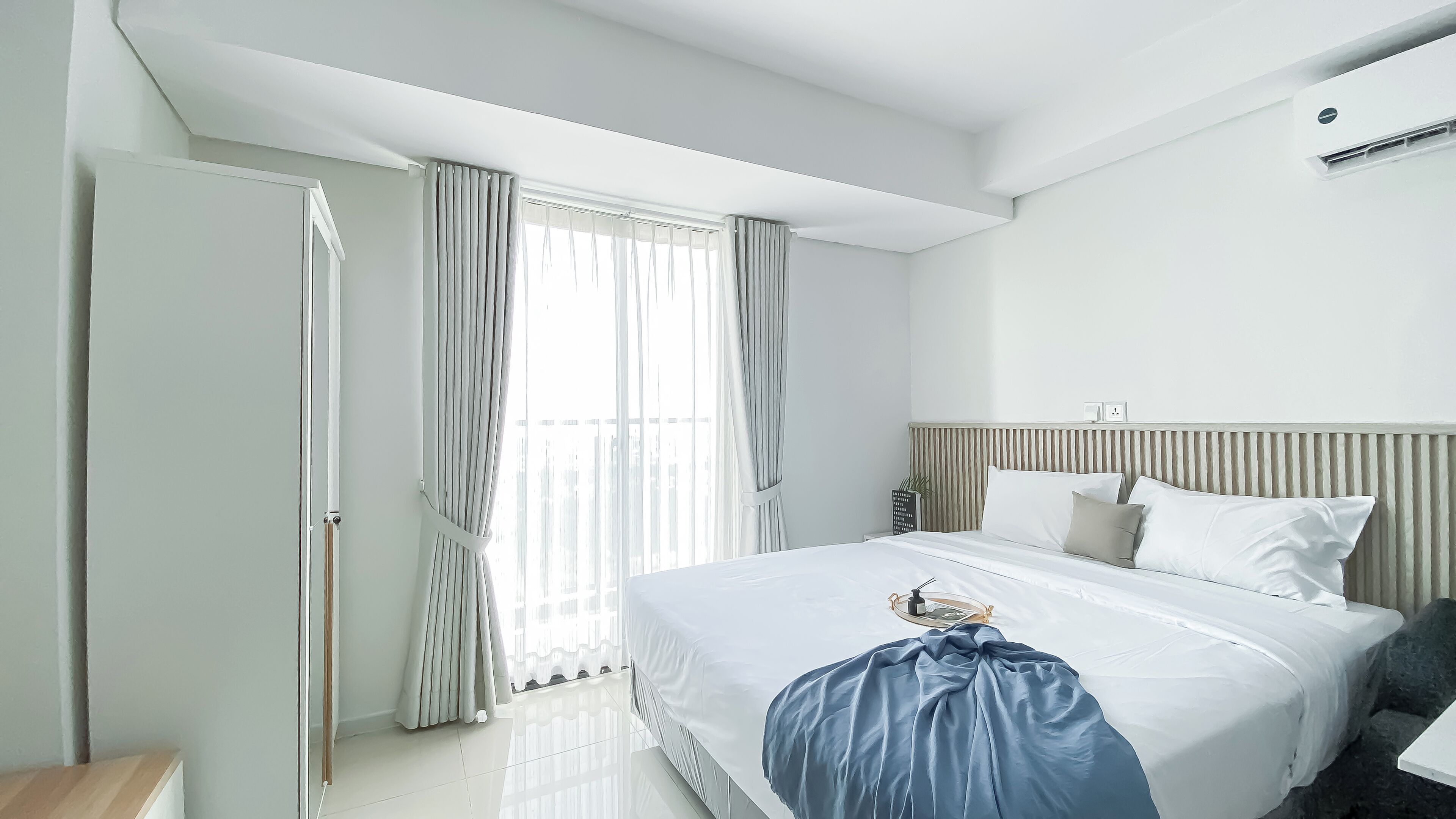 A modern hotel room with a large bed, a bedside table, a wardrobe, and a window with curtains.