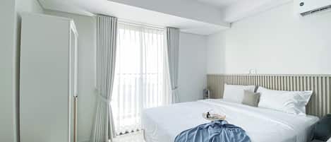 A modern hotel room with a large bed, a bedside table, a wardrobe, and a window with curtains.
