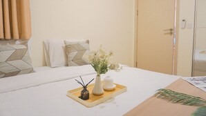 Ein ordentlich bezogenes Bett mit einem Tablett, auf dem eine Blumenvase, eine Kerze und ein kleines dekoratives Objekt stehen.