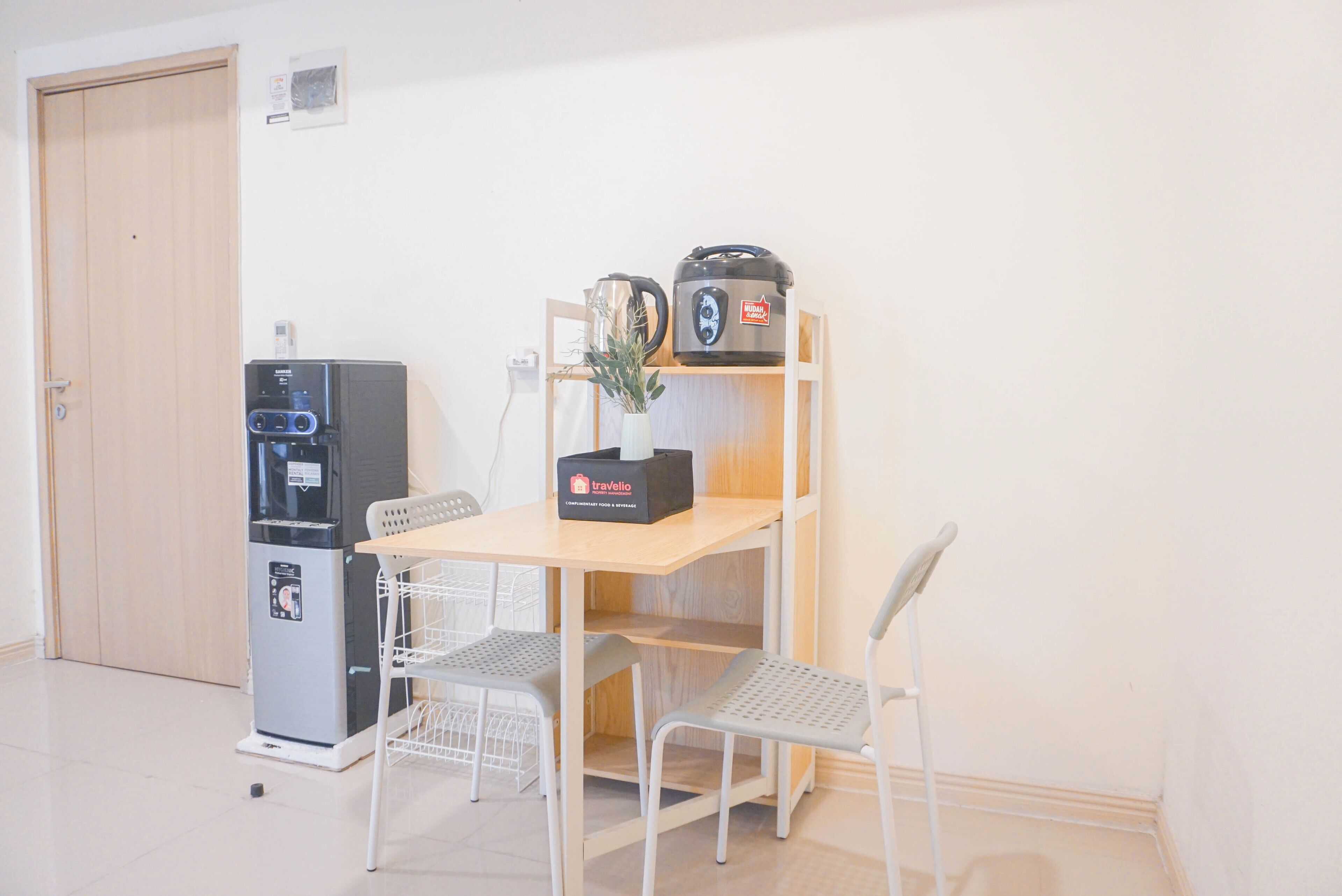 A small kitchenette with a refrigerator, a coffee maker, and a travel case on a wooden shelf.