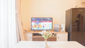 Ein Zimmer mit Fernseher, der ein Sportevent zeigt, einer weißen Vase mit Blumen und einem Holzschrank.