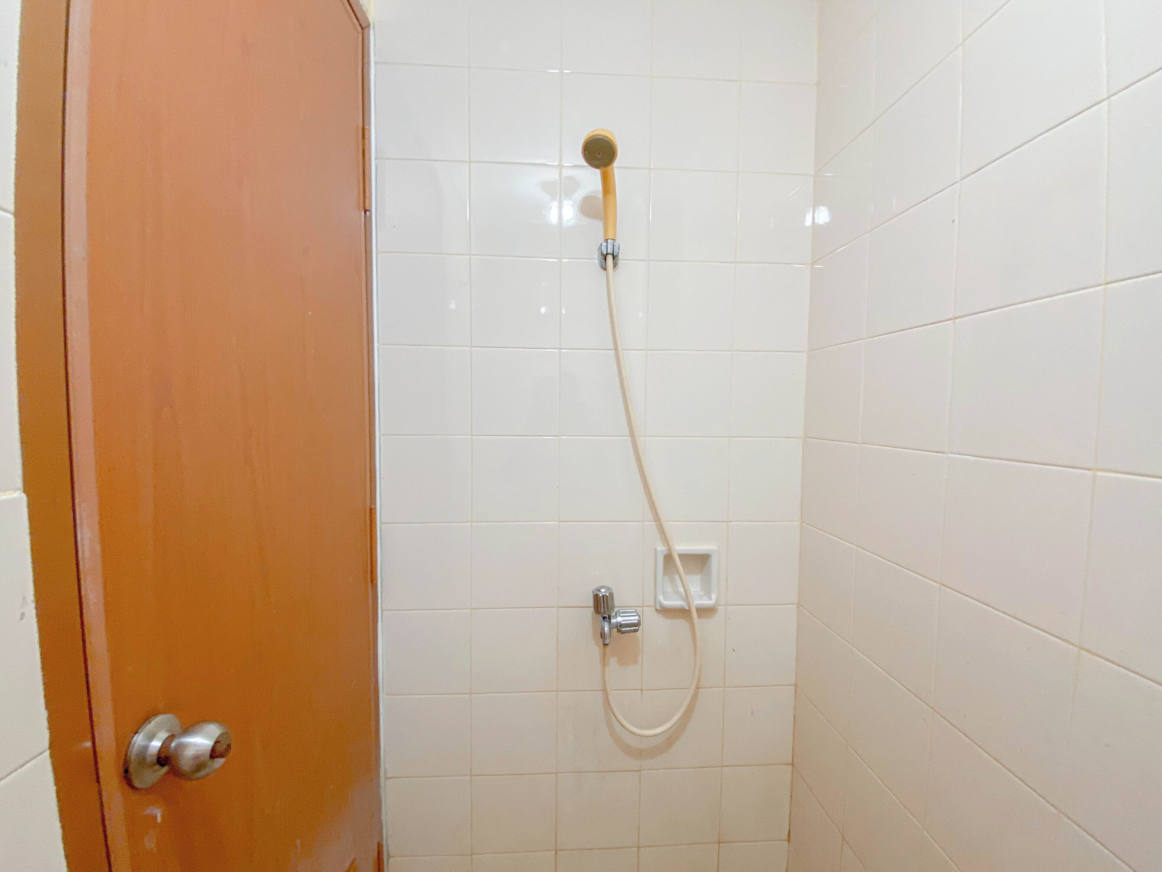 A bathroom with white tiled walls, a wooden door, and a shower with a handheld showerhead and a wall-mounted faucet.