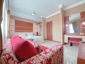 A bedroom with a bed, a red and white patterned sofa, a large mirror, and a wardrobe. - The Signature Suite 3Br At Galeri Ciumbuleuit 1 Apartment (Bandung)