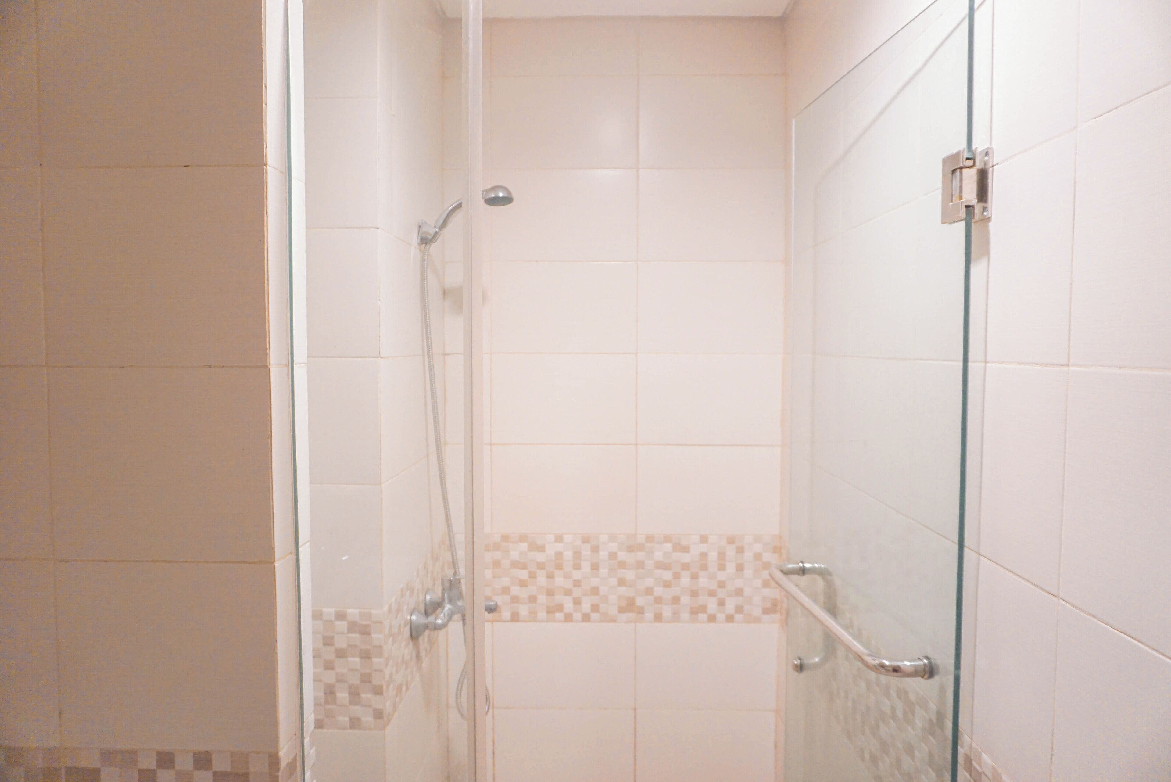 A shower with a glass door, a handrail, and a tiled wall with a checkered pattern near the floor.
