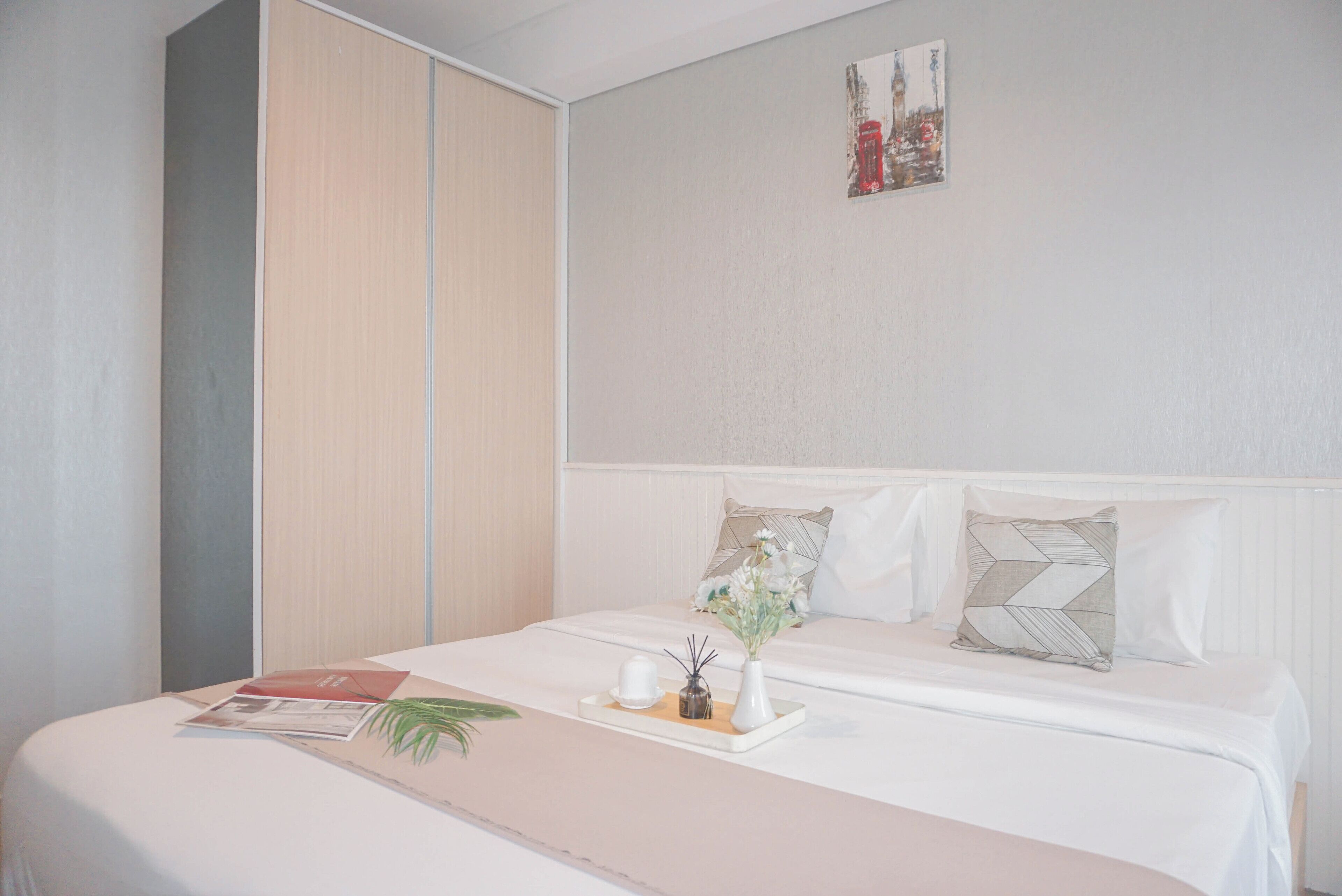 Un lit bien fait, avec une petite table sur laquelle sont disposés des articles de toilette, un petit vase avec des fleurs et un magazine sur la table de chevet.
