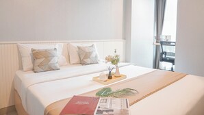 Habitación de hotel con una cama grande, dos almohadas, una bandeja con un florero y velas, una revista y un ventanal con cortinas.