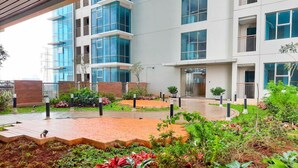 Un edificio moderno de varios pisos, con amplios ventanales y un patio ajardinado con senderos y vegetación.