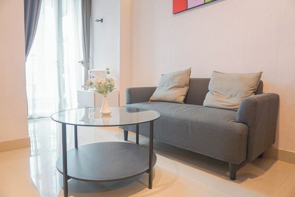 A modern living room with a grey sofa, two cushions, a glass coffee table, and a vase with flowers.