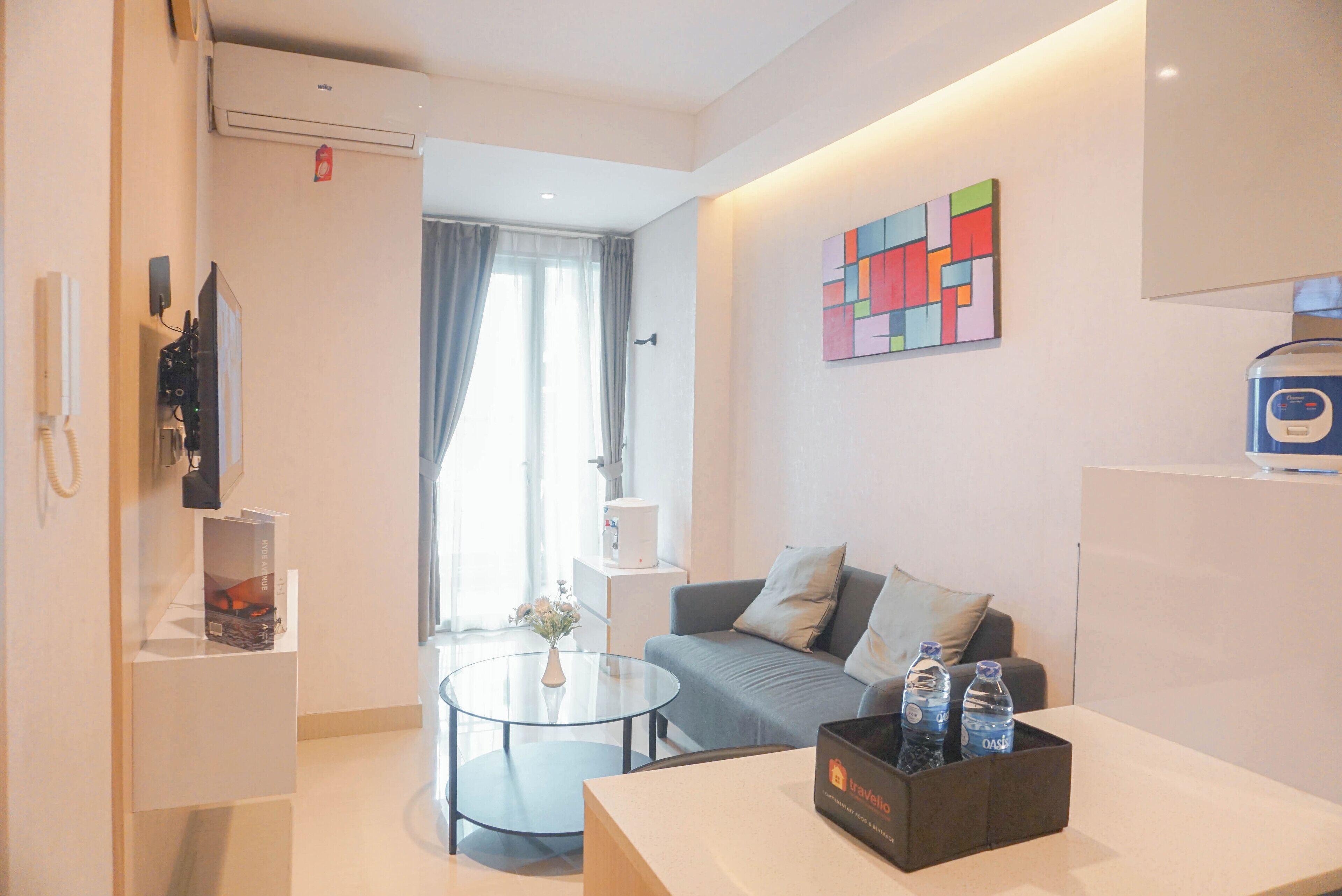 Una moderna camera d'albergo con divano, tavolino in vetro, piccolo comodino, un quadro appeso e un minibar.