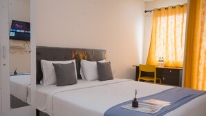 A neatly made bed with a blue accent, a desk with a chair, and a TV mounted on the wall. - Convenient Studio Apartment At B Residence (Pagedangan)
