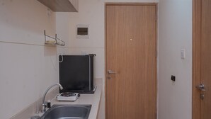 A small kitchenette with a sink, stove, and a microwave. - Convenient Studio Apartment At B Residence (Pagedangan)