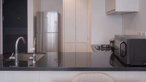 A modern kitchen with a stainless steel refrigerator, a microwave, and a black countertop.