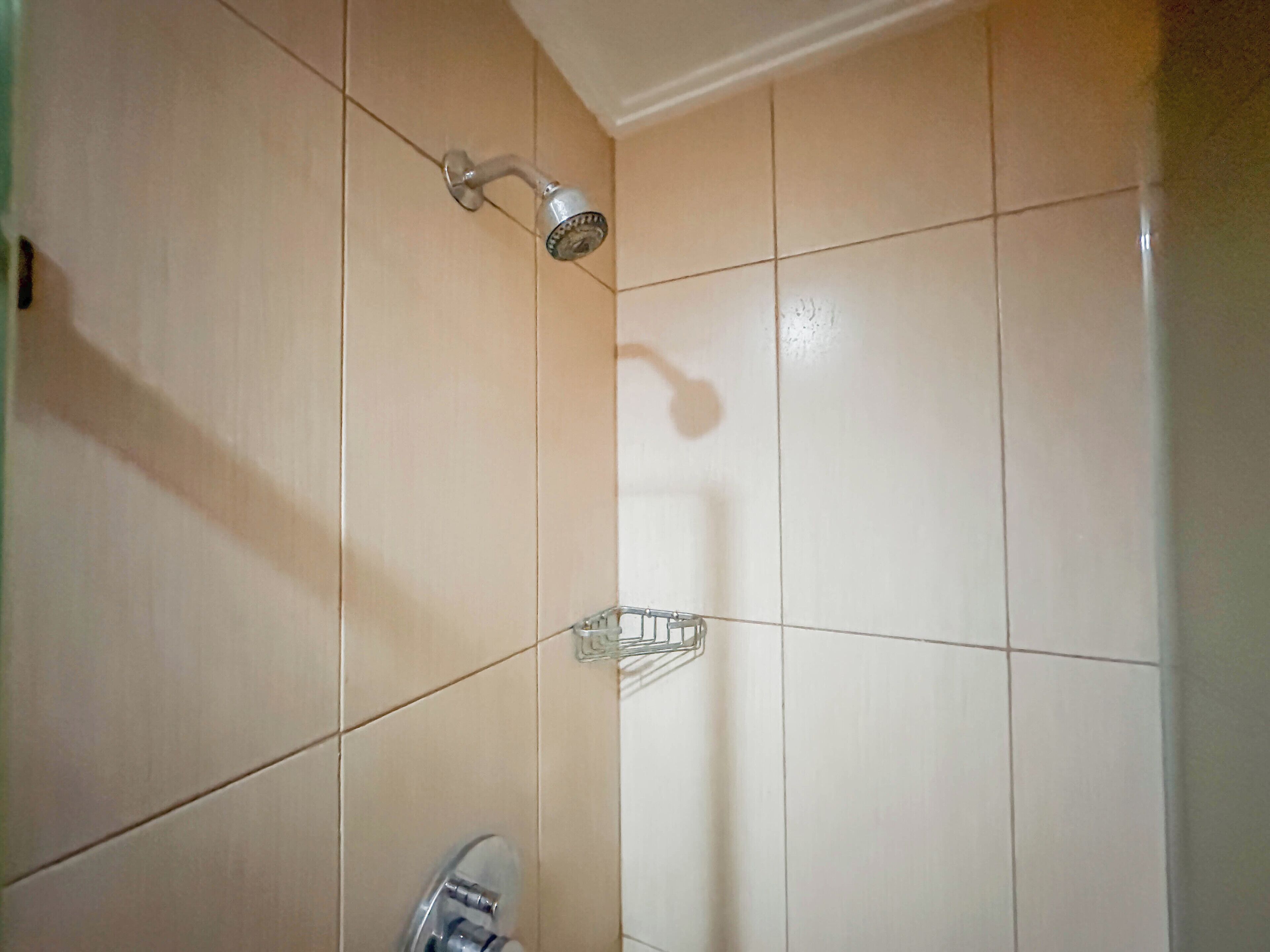 Ein Badezimmer mit beigen Fliesen, einer Duschbrause und einer transparenten Glasablage.