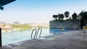 An outdoor infinity pool with a city view, a stone wall, and a few trees. - Best Price And Relaxing Studio (No Kitchen) At Tamansari Papilio Apartment (Surabaya)