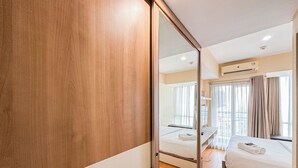 A hotel room with a wooden wardrobe, a bed with white linens, a bedside table, and a window with curtains. - Best Price And Relaxing Studio (No Kitchen) At Tamansari Papilio Apartment (Surabaya)