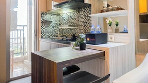 A modern kitchen with a tiled backsplash, a built-in stove, and a countertop with water bottles and a box labeled "Travelio". - Best And Homey 2Br At Bassura City Apartment (Jakarta)