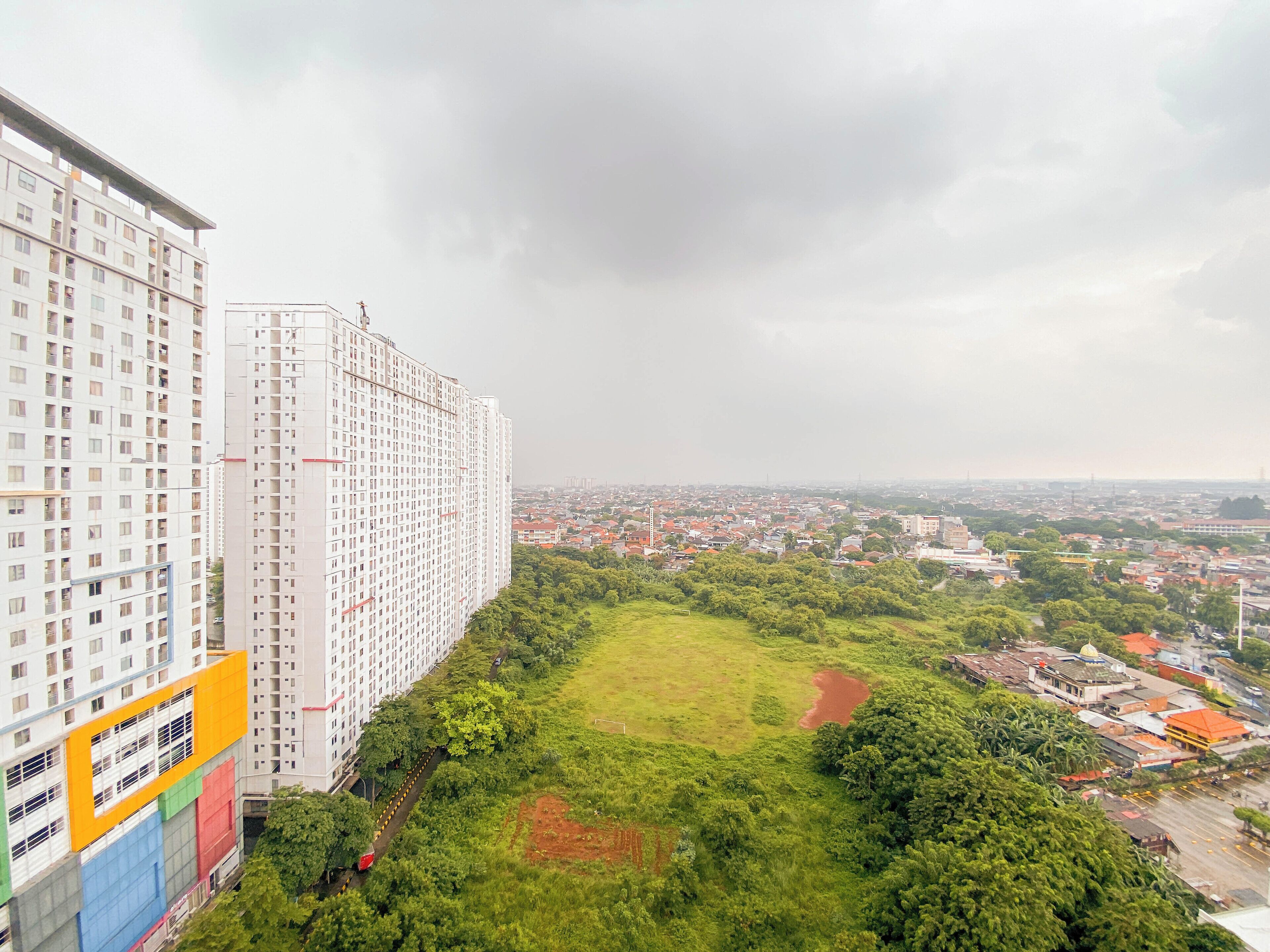 A high-rise building with multiple floors and balconies, surrounded by greenery and a view of a cityscape.