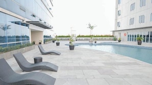 Uma área de piscina no terraço, com espreguiçadeiras e plantas em vasos.