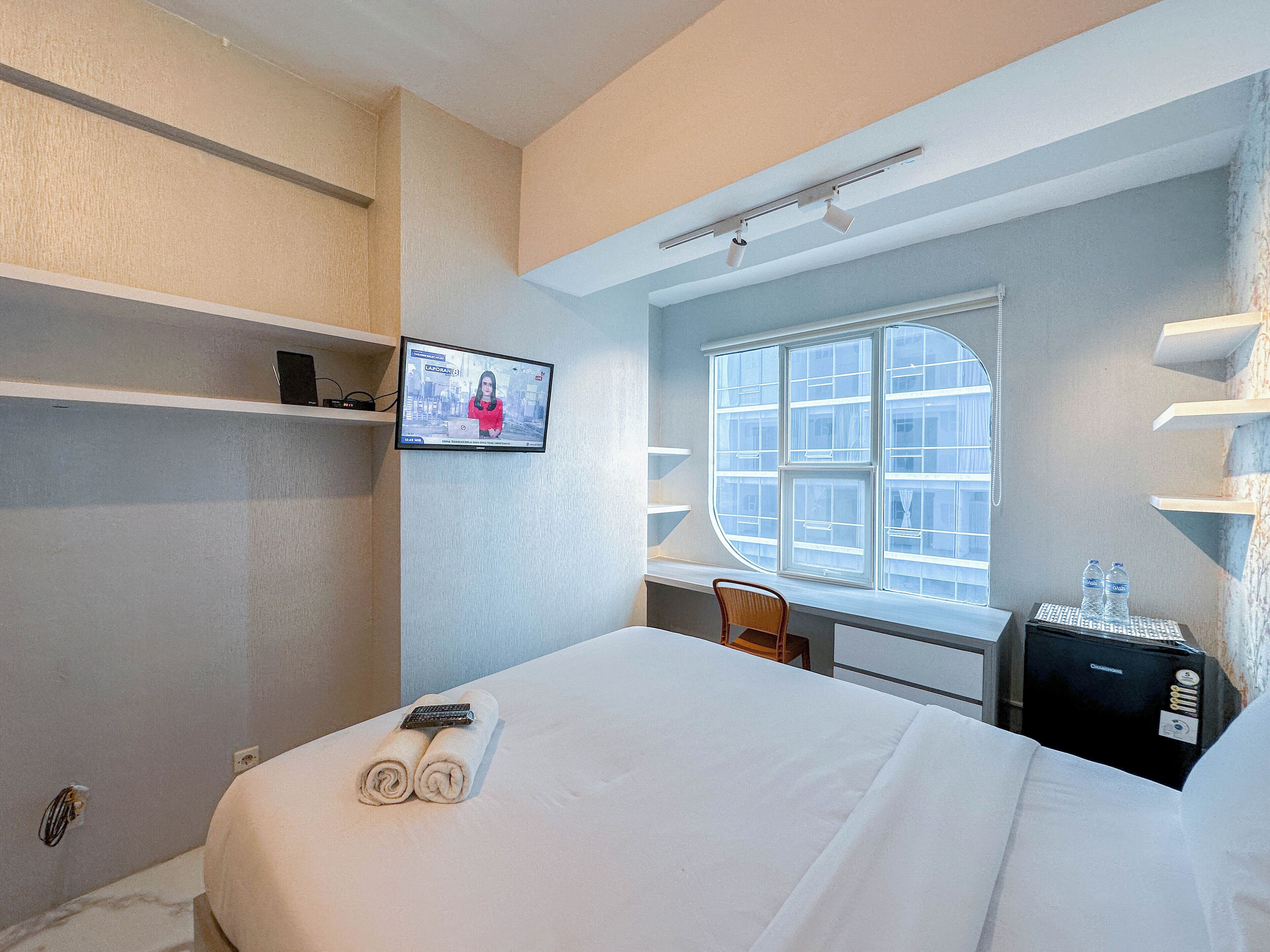 Habitación de hotel con cama, escritorio, silla, televisor y ventana con persianas.
