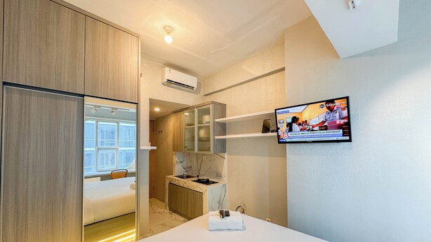 Quarto de hotel com cama, televisão na parede, escrivaninha com cadeira e guarda-roupa.