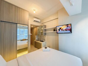 A hotel room with a bed, a TV mounted on the wall, a desk with a chair, and a wardrobe.