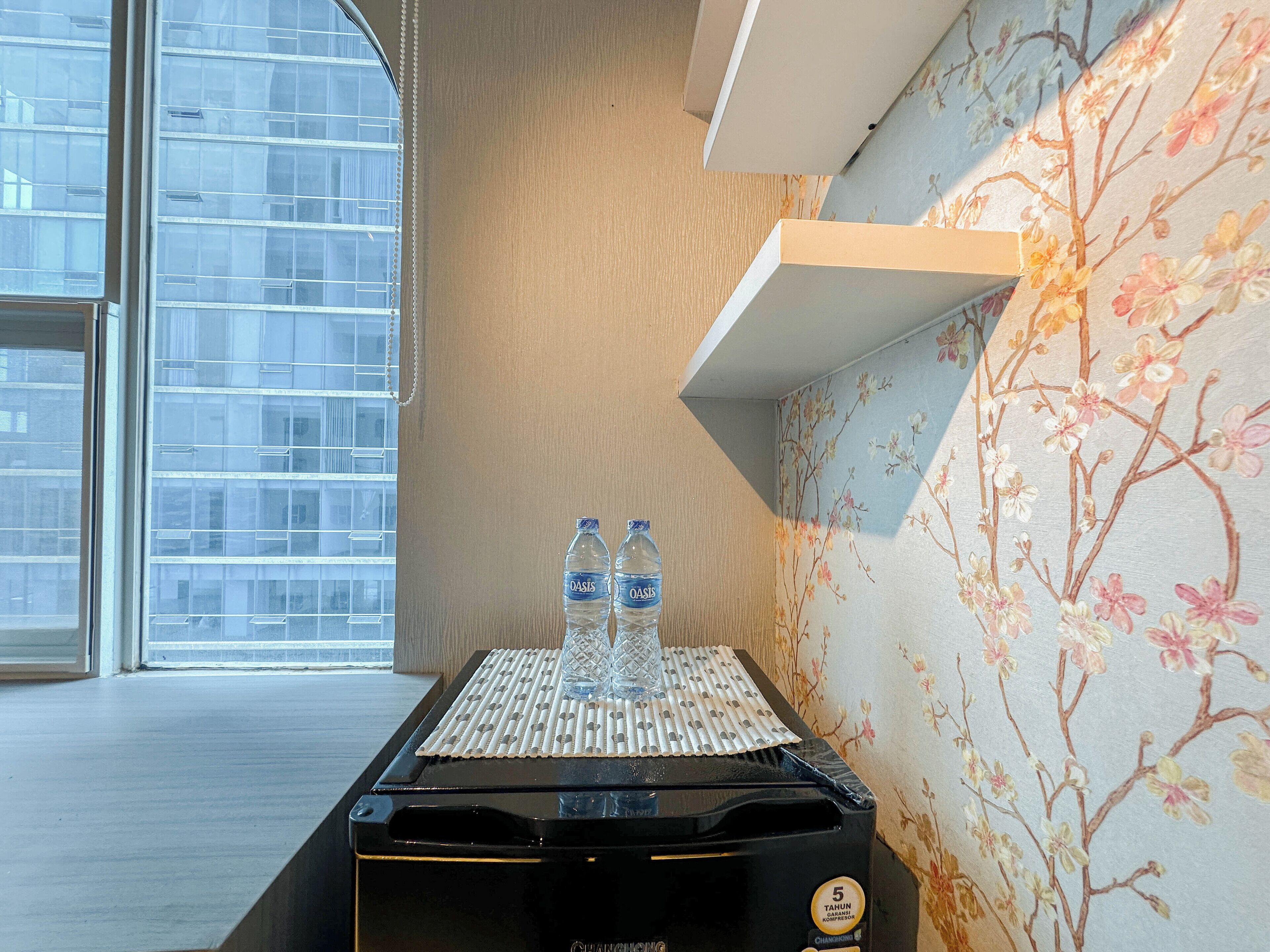 A minibar with two water bottles, a black container, and a floral wallpaper.