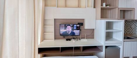 A hotel room with a bed, a TV mounted on a wooden wall, and a small shelf with a remote control.