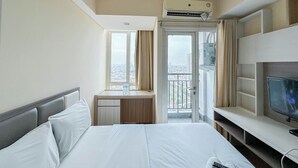 Habitación de hotel con cama, escritorio, televisor y balcón con vista a la ciudad.