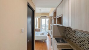 Un pasillo estrecho que conduce a un dormitorio con balcón, una kitchenette con salpicadero de azulejos y un ventanal con cortinas.