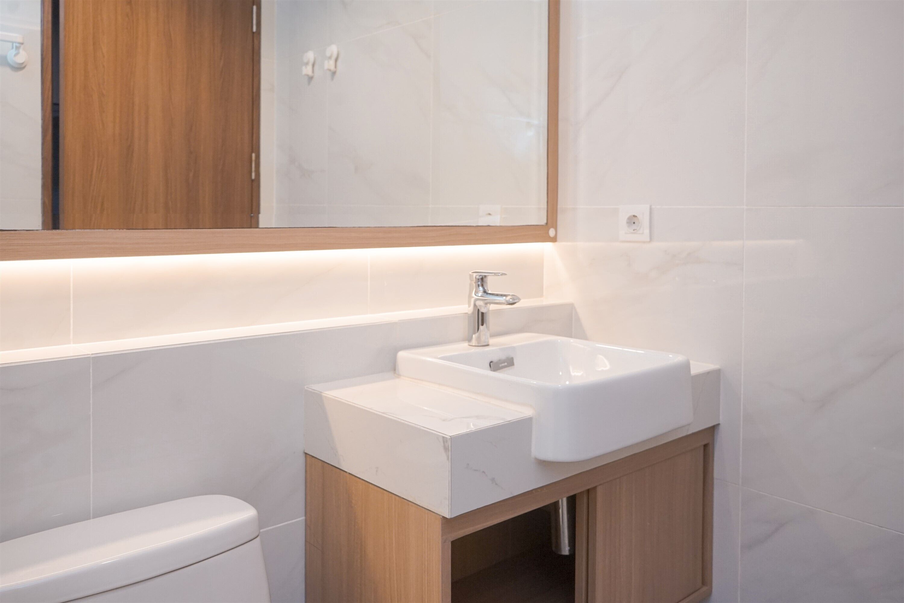Un baño moderno con un lavabo blanco, un mueble de madera y un espejo sobre el lavabo.
