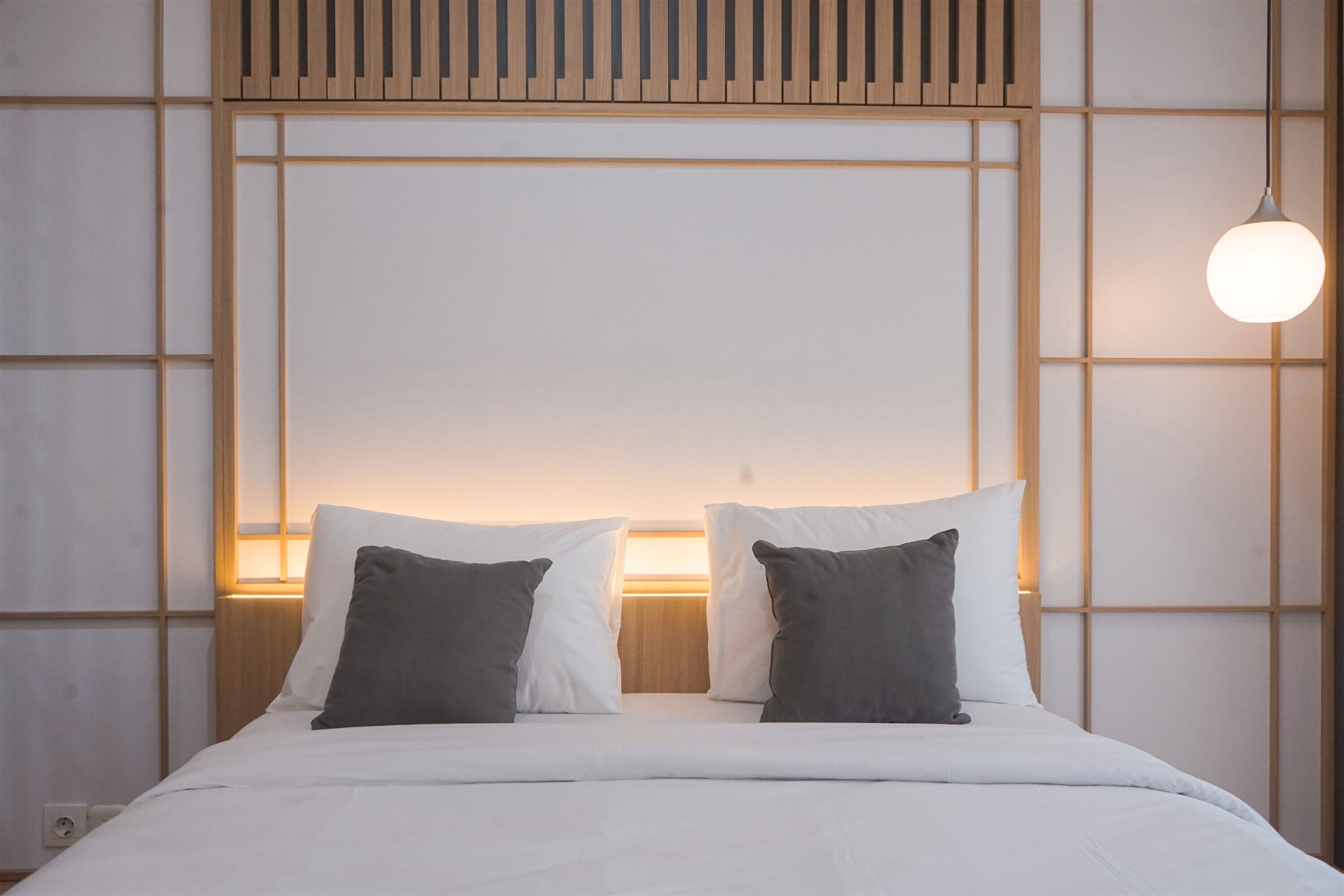 A neatly made bed with white and gray bedding, a wooden headboard, and a hanging light fixture.