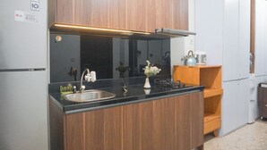 A kitchen with a black countertop, wooden cabinets, a stainless steel sink, and a built-in oven. - Elegant And Best Deal 1Br At L'Avenue Pancoran Apartment (Jakarta)