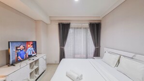 Ein Hotelzimmer mit Bett, Fernseher auf einem weißen Schrank und einem Fenster mit Vorhängen.