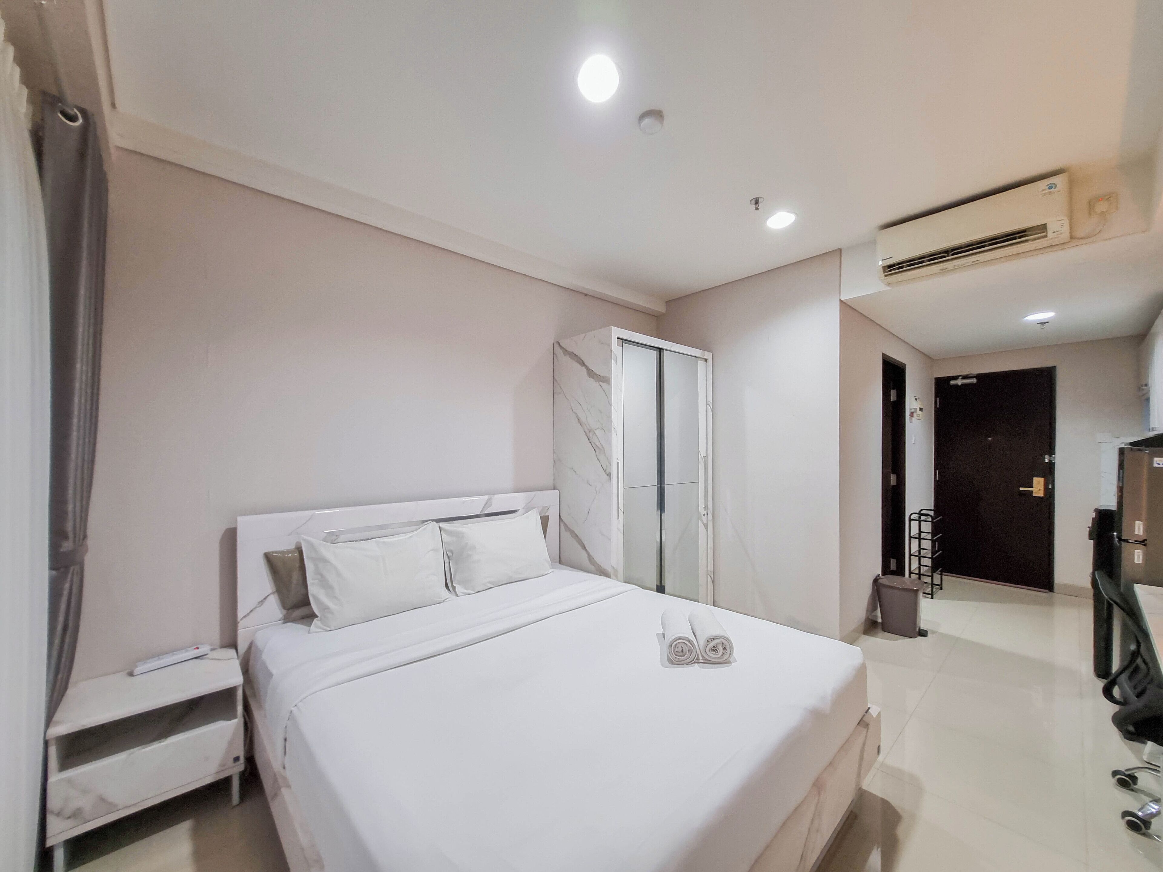 A modern hotel room with a large bed, a wardrobe, a desk, and an air conditioning unit.