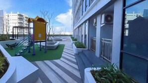 A modern building with a rooftop garden, outdoor seating area, and a children's play structure. - The Simply Look 1Br Apartment At Delft Ciputra Makassar (Makassar)