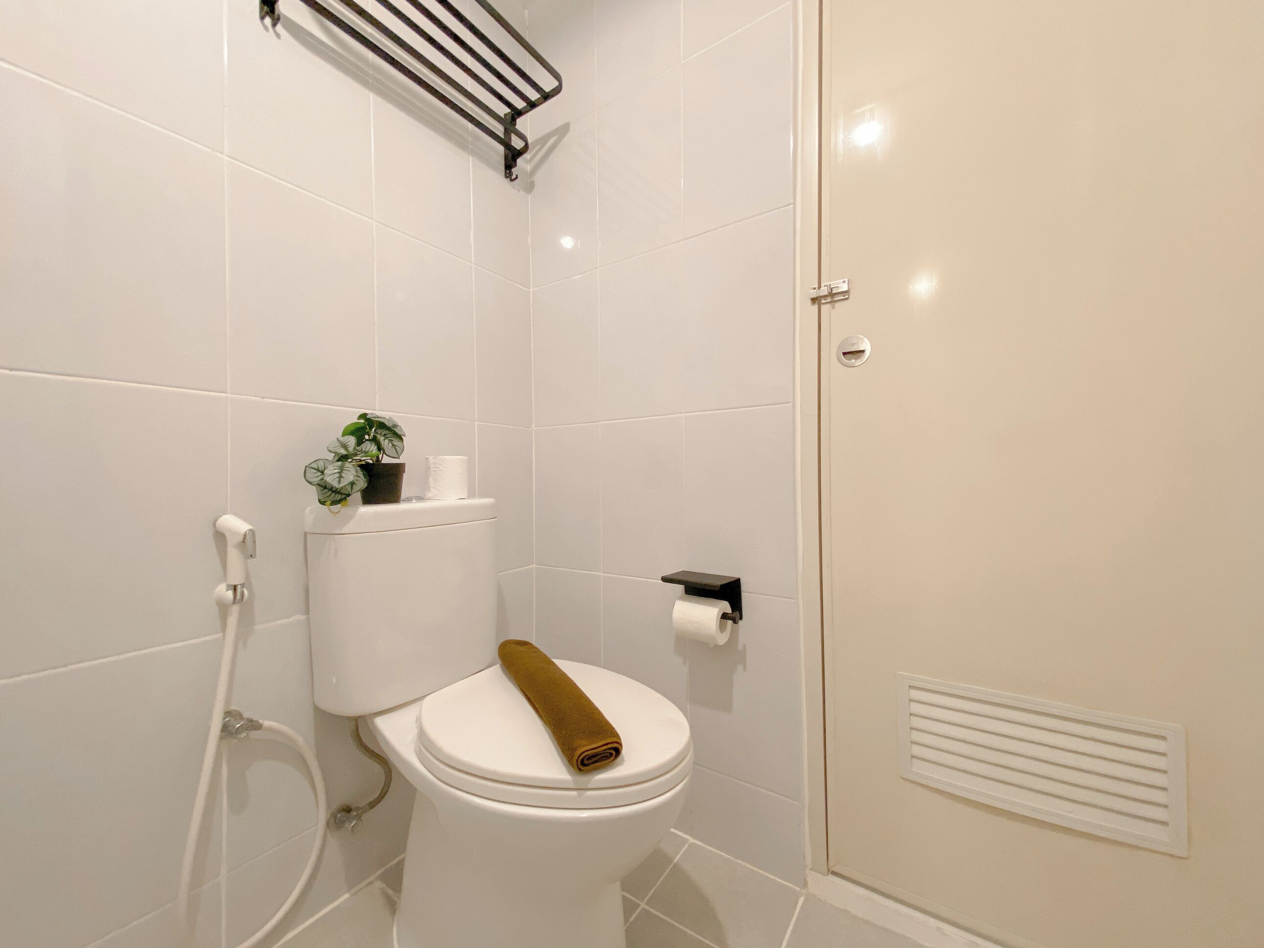 Une salle de bain moderne avec des carreaux blancs, des toilettes avec un porte-serviette, un porte-rouleau de papier toilette et un panneau de commande de la douche.
