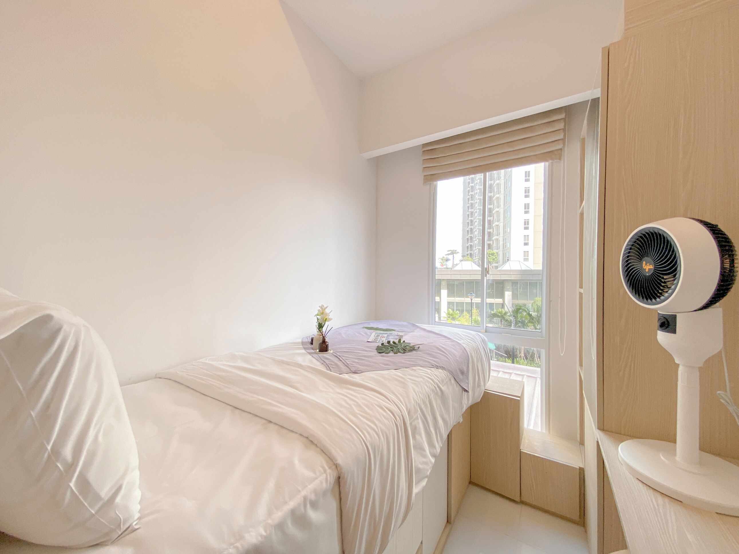 Un dormitorio con una cama, una ventana con persianas, un ventilador y una planta pequeña en el alféizar.