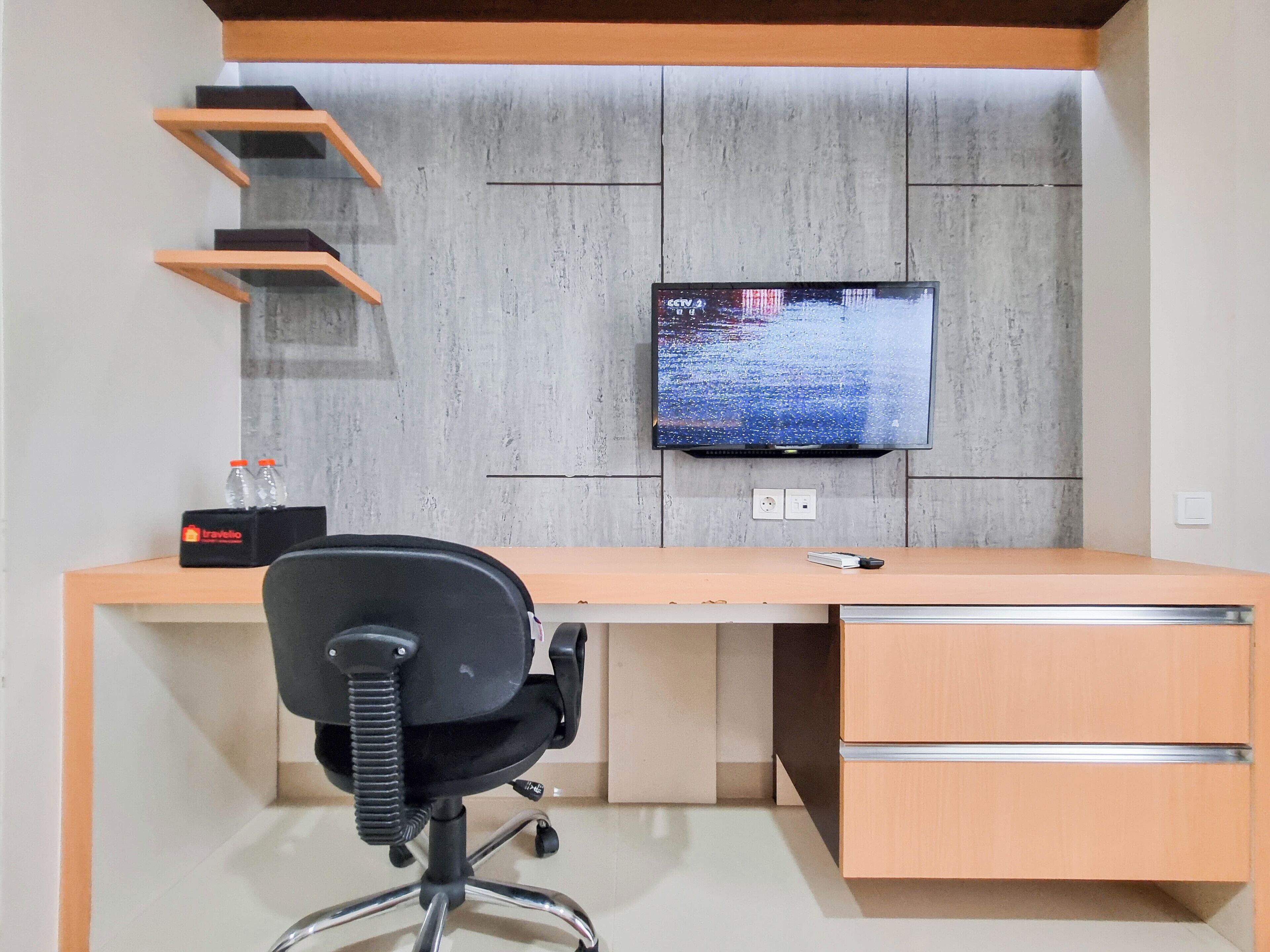 A modern office desk with a computer, a chair, and a TV mounted on the wall.