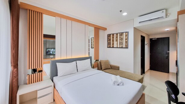 A modern hotel room with a large bed, a desk, a chair, and an air conditioning unit.
