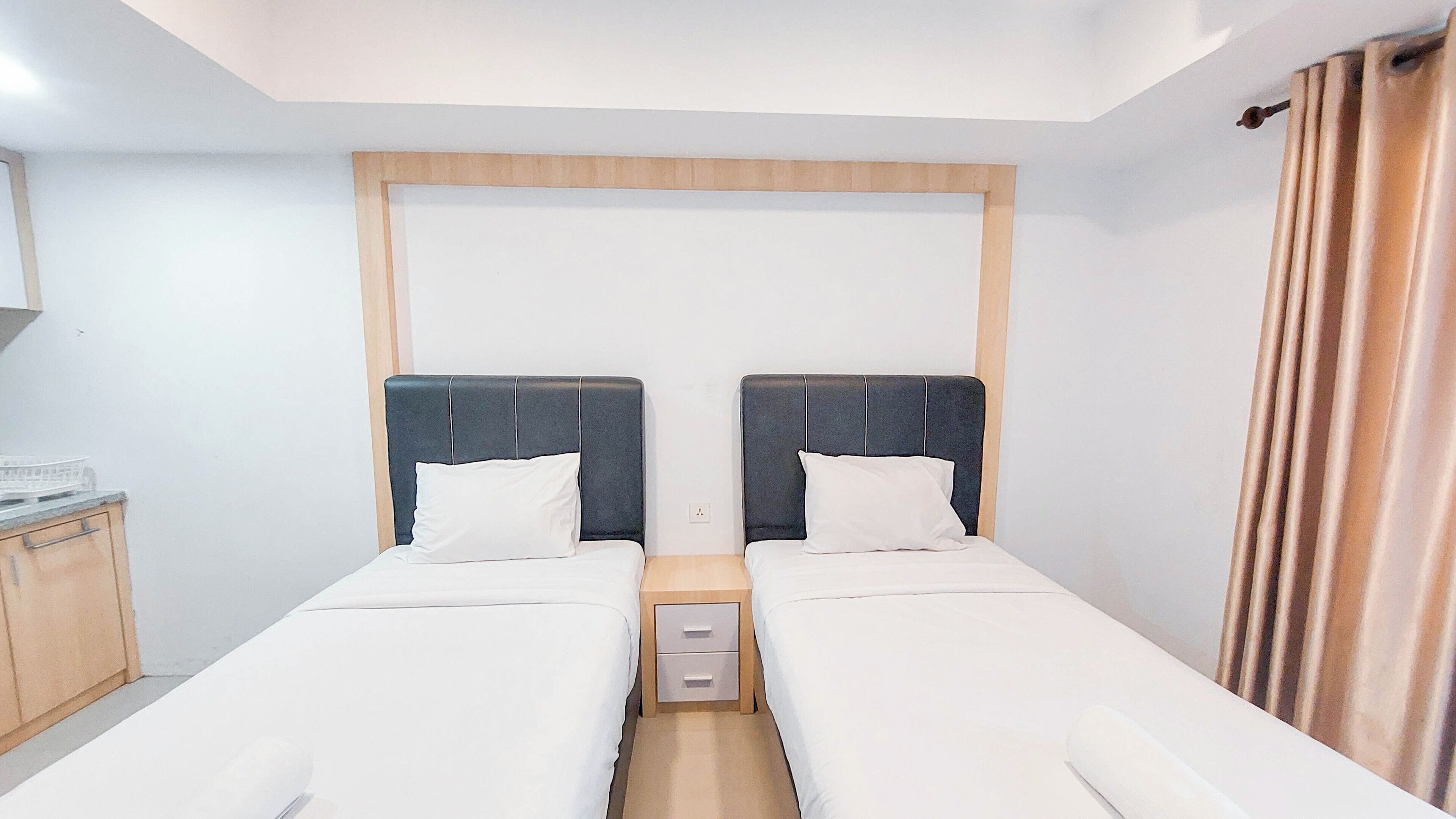 Ein Doppelzimmer mit zwei Einzelbetten, einem hölzernen Kopfteil, einem kleinen Nachttisch mit Schubladen und einem Vorhang auf der rechten Seite.