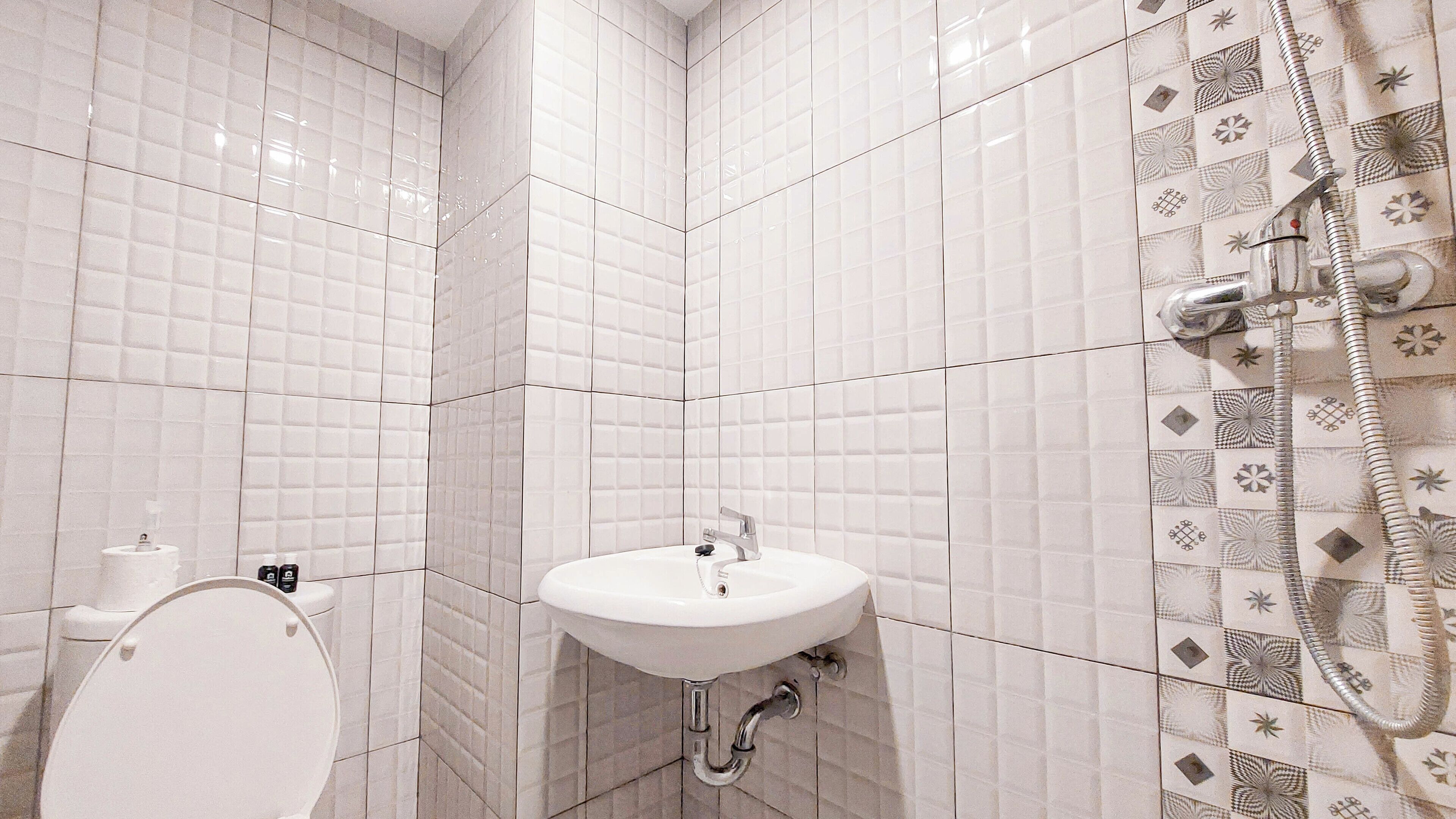 A bathroom with white subway tiles, a white sink, a toilet, and a shower with patterned tiles.