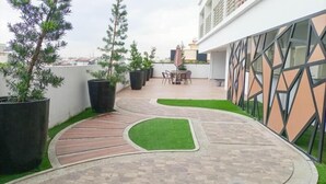 Un patio en la azotea con un sendero curvo, plantas en macetas y una zona de estar.