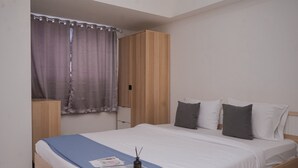 Ένα υπνοδωμάτιο με ένα κρεβάτι με ξύλινο πλαίσιο, ένα μπλε κάλυμμα κρεβατιού και ένα παράθυρο με κουρτίνες.