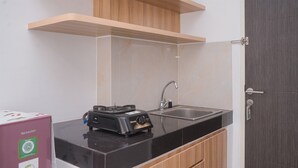 A compact kitchen with a black countertop, a stainless steel sink, and wooden cabinets. - Simply And Homey Studio Room Serpong Garden Apartment (Cisauk)