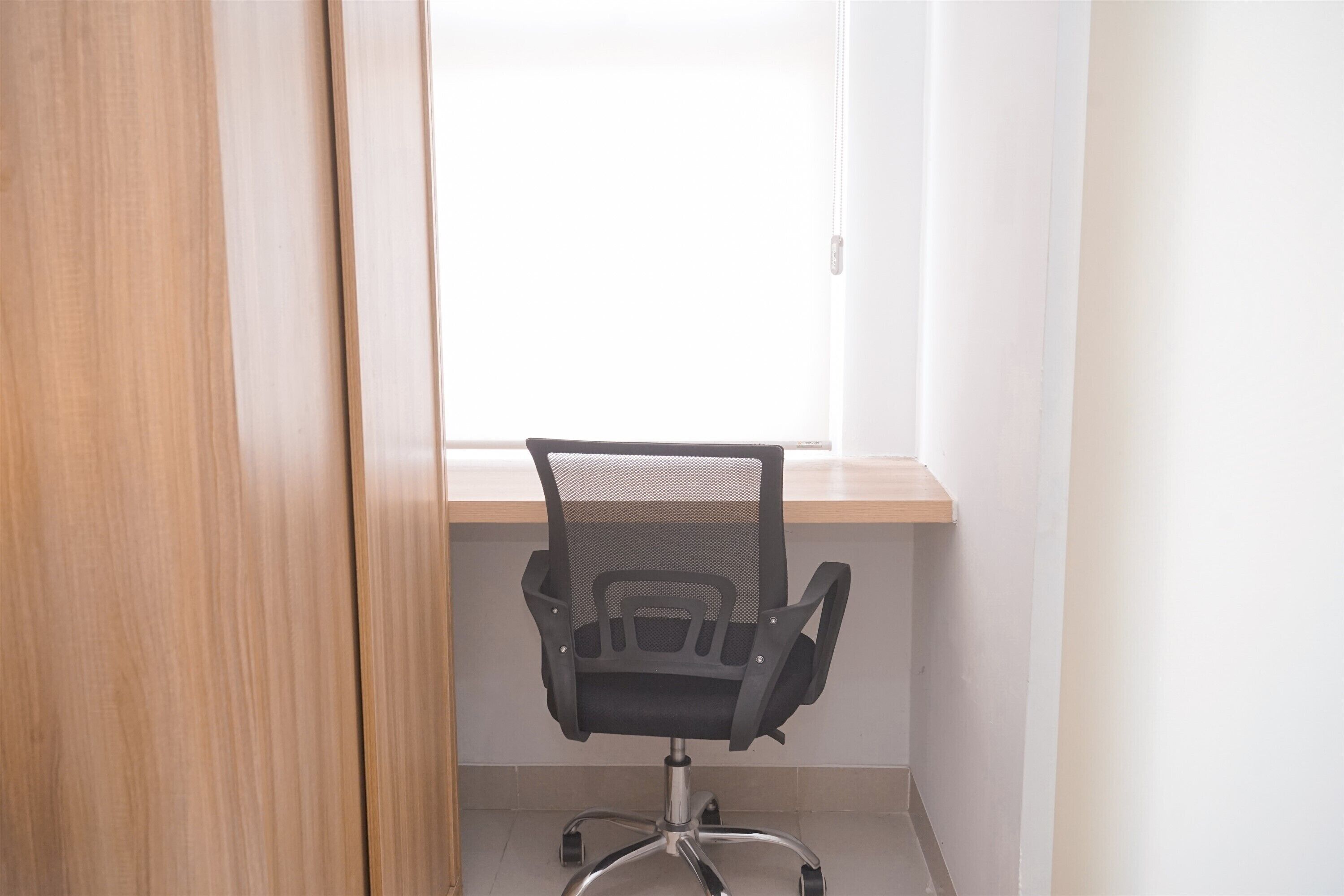 Ein Büro im Eck mit Fenster, einem Holztisch und einem schwarzen Bürostuhl.