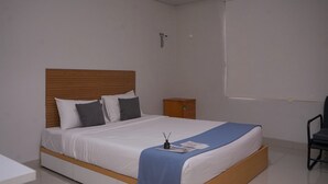 Een opgemaakt bed met een houten hoofdbord, een klein nachtkastje en een stoel.