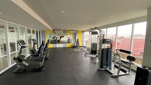 Een sportschool met cardioapparatuur, gewichten en grote ramen met uitzicht op gebouwen.