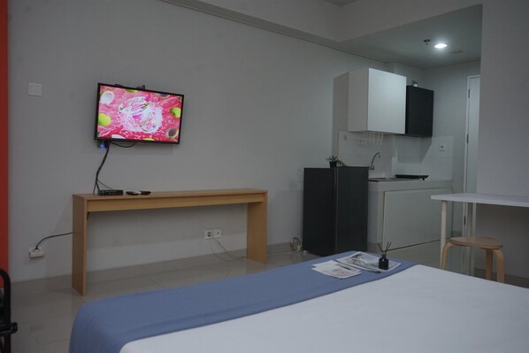Una habitación con cama, escritorio, televisor y kitchenette.